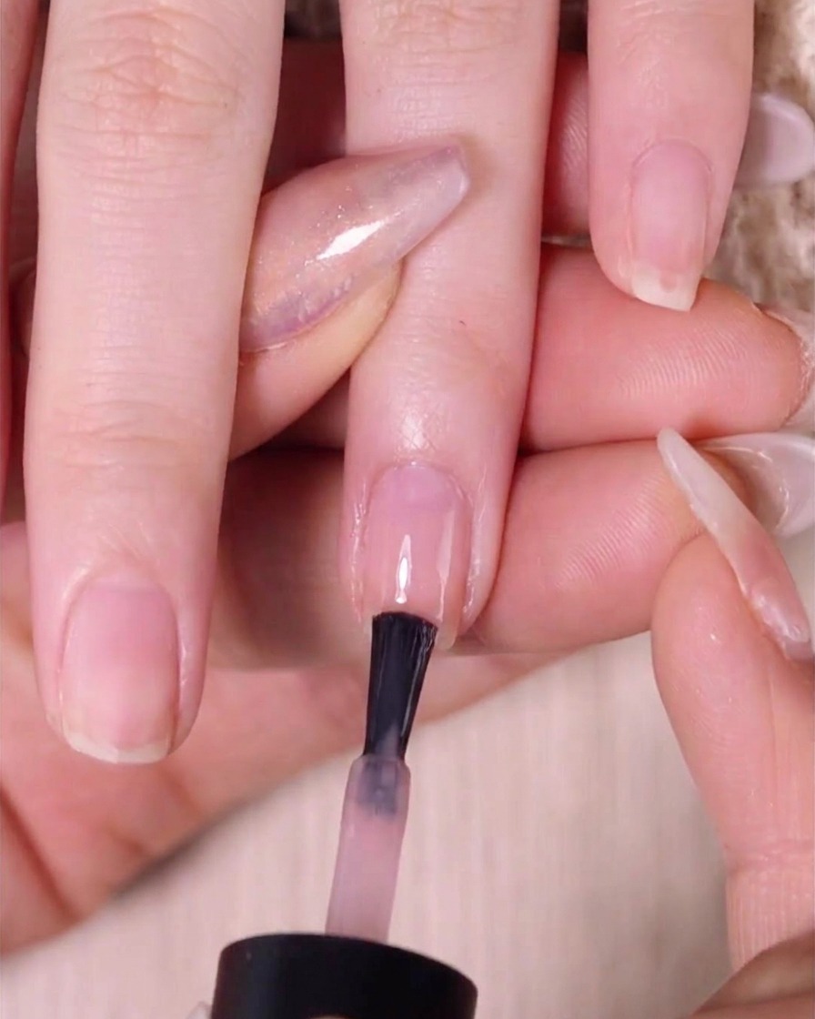 Pędzelek nakładający drugą warstwę lakieru nude pink na górną połowę paznokcia.