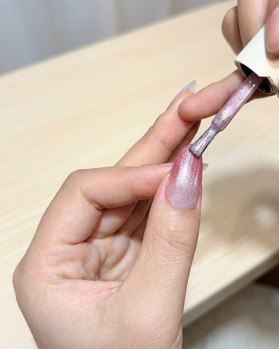 Pędzelek nakładający warstwę lakieru cat-eye na bazę ombre w kolorze magenty.
