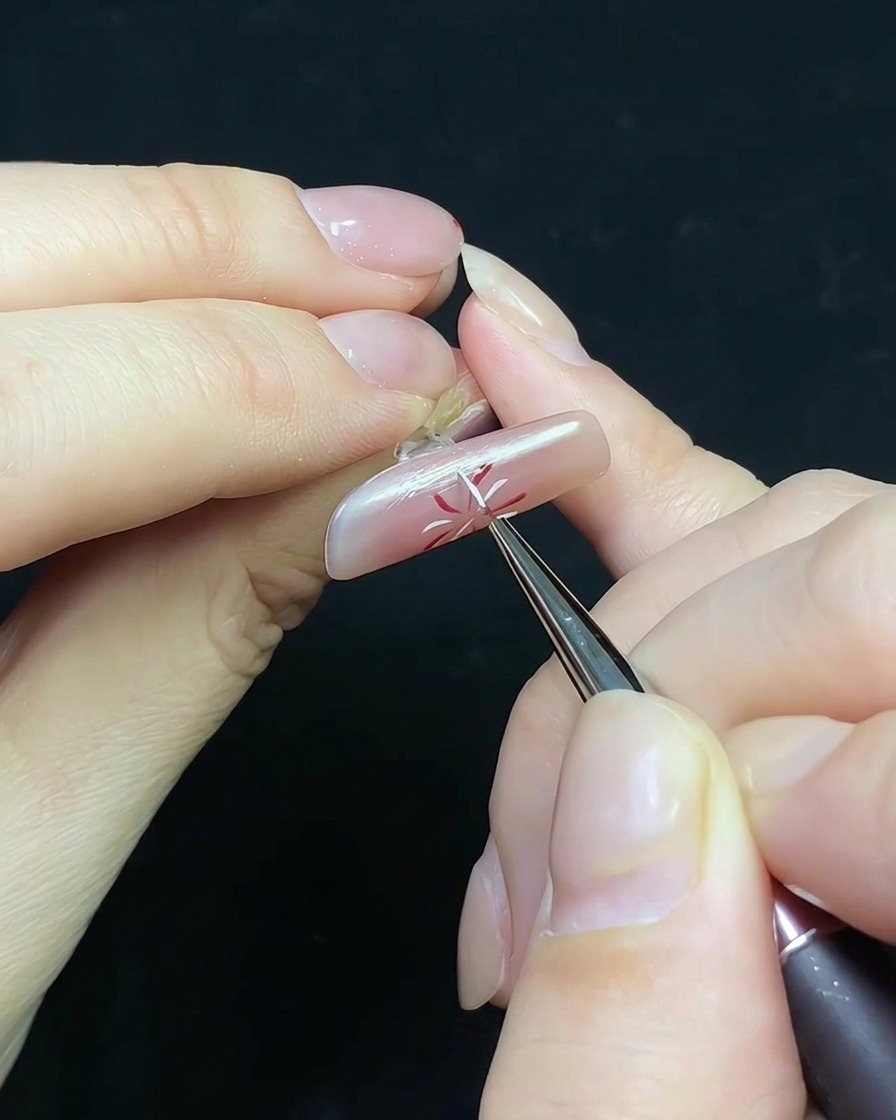 Cienki pędzelek nakładający top coat na paznokieć z wzorem fajerwerka i małą ozdobą perłową.