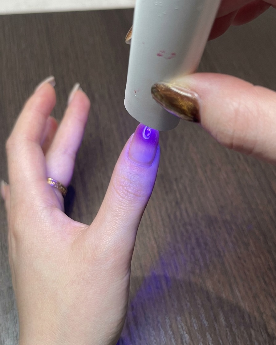Dłoń pod małą lampą UV, utwardzająca gotowy wzór magnetyczny cat eye.