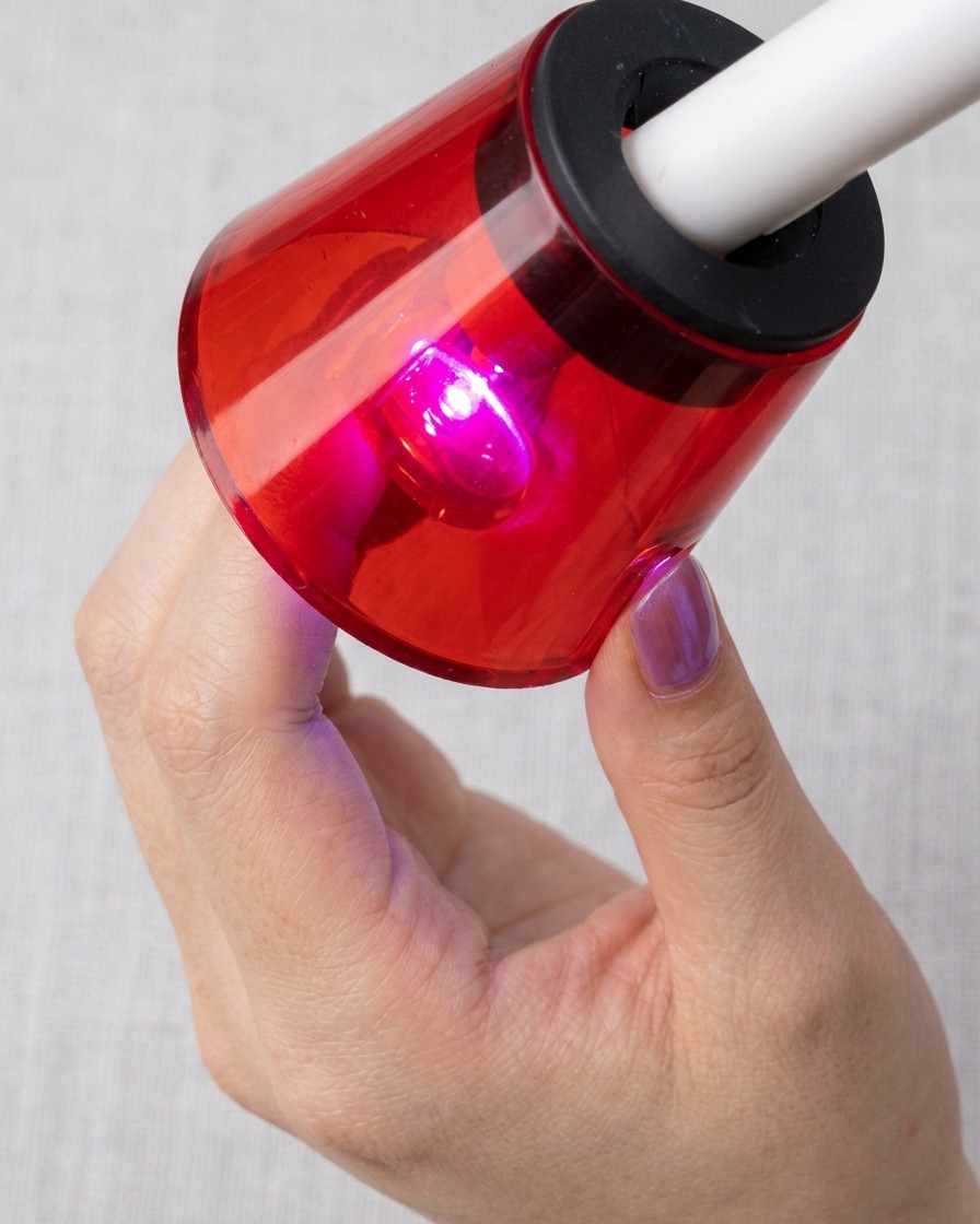 Paznokieć umieszczony pod czerwoną lampą UV/LED, utwardzany z widocznymi magnetycznymi cząsteczkami kociego oka.