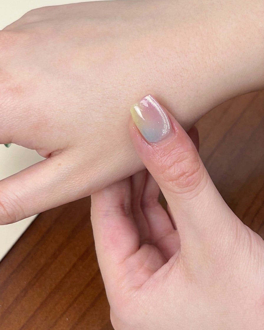 Zbliżenie na dłoń z gotowym, kolorowym manicure gradientowym spoczywającą wewnątrz włączonej lampy UV/LED.