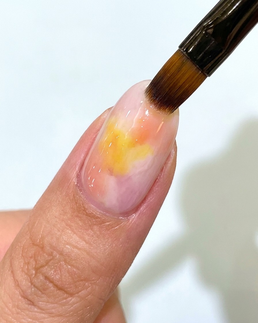 Pędzelek nakładający przezroczysty matowy top coat na paznokieć z różowo-żółtym ombre.