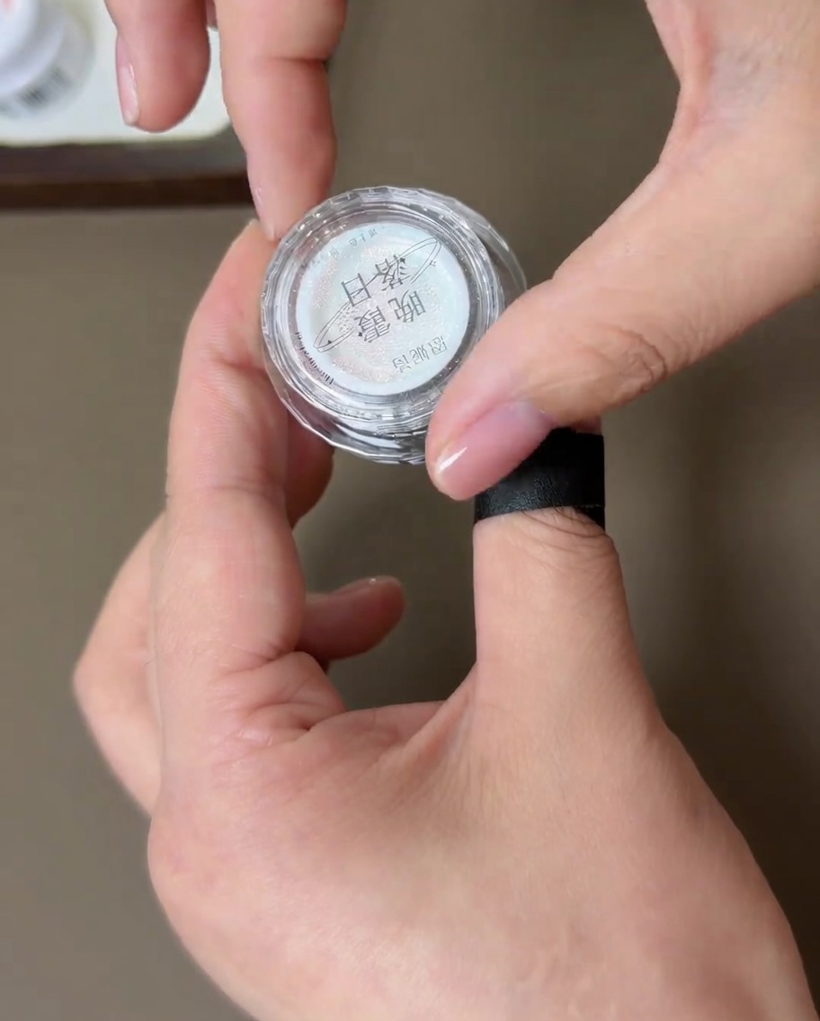 Mały pojemnik z pyłkiem sunset aurora chrome trzymany dłonią z gotowym manicure, pokazujący teksturę pyłku.