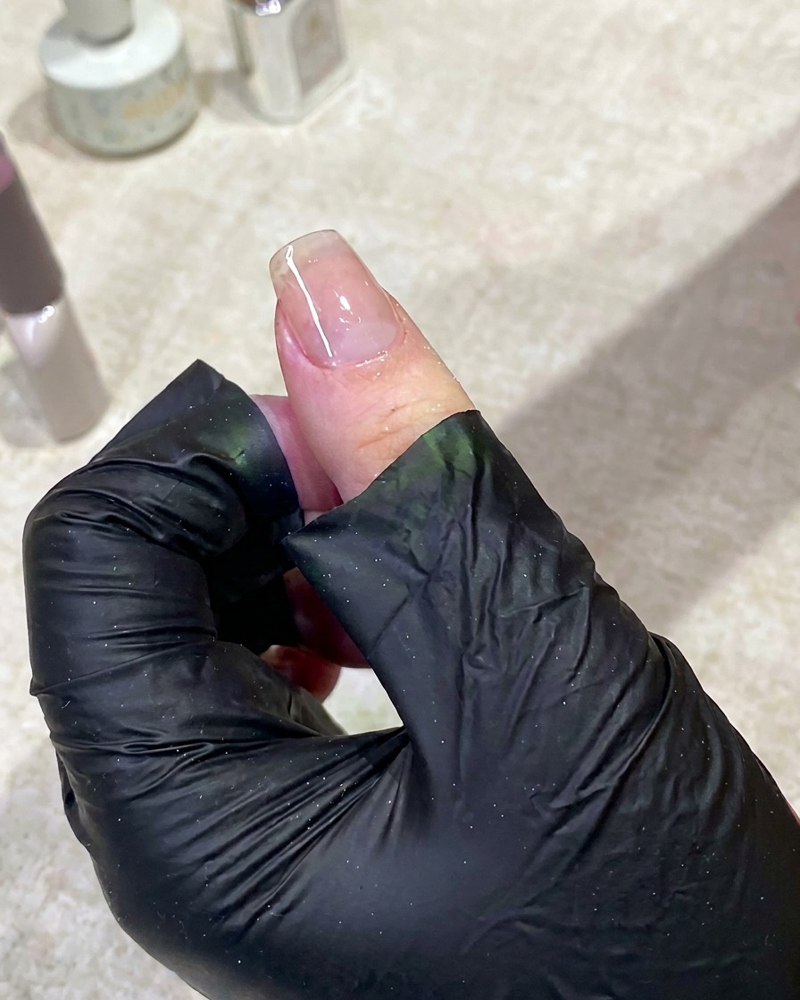 Dłoń ułożona wewnątrz lampy UV z włączonym światłem, utwardzająca bazę pod manicure.