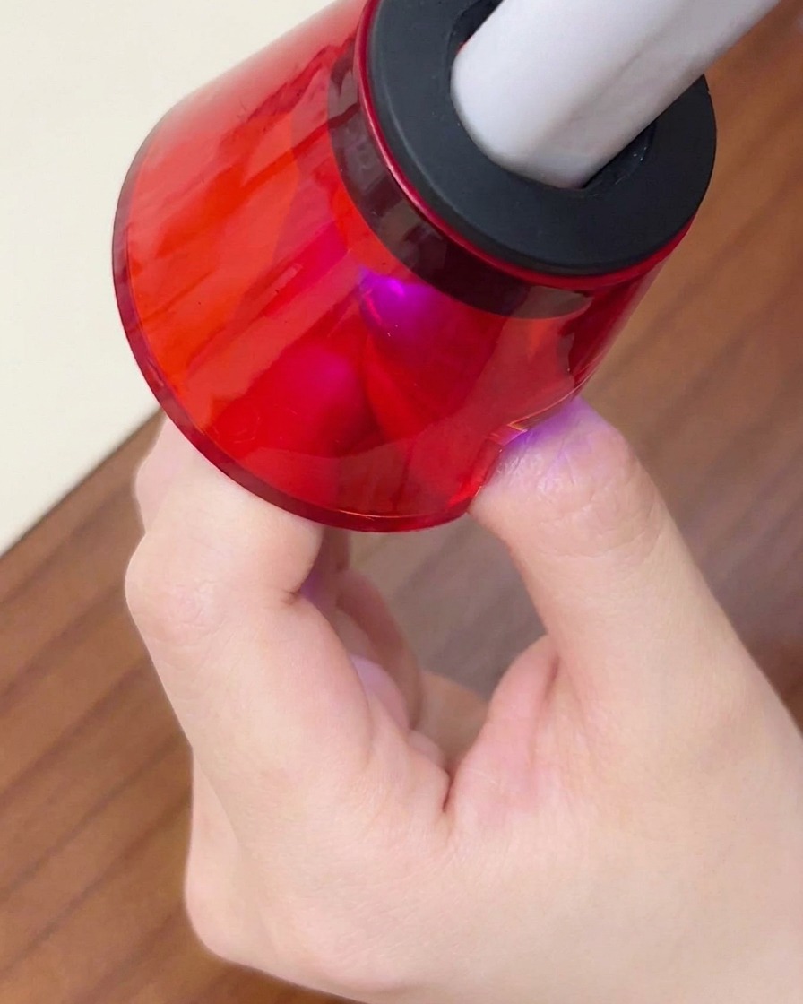 Zbliżenie palca umieszczonego pod mini, czerwoną przenośną lampą UV/LED w celu końcowego utwardzenia.