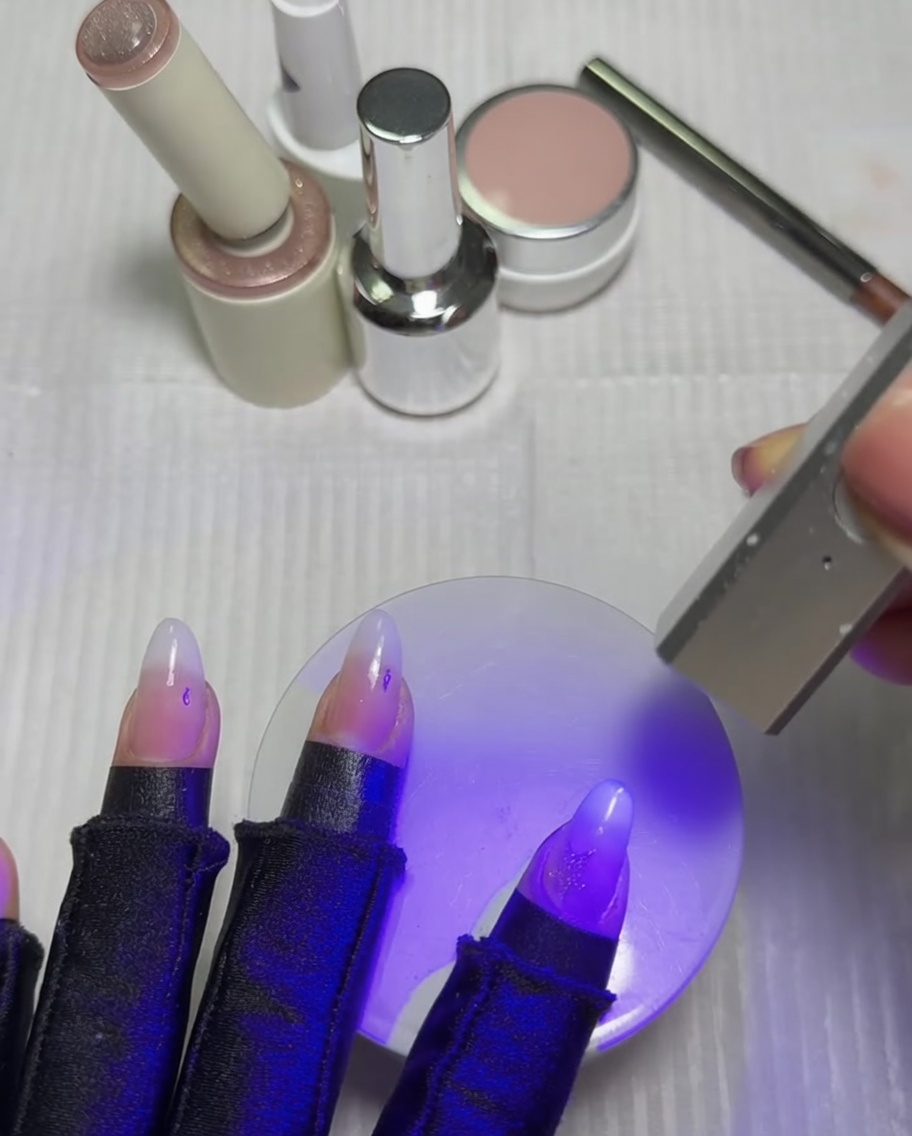 Paznokcie spoczywające pod fioletową lampą UV/LED w celu utwardzenia aktywowanej gwiazdki.