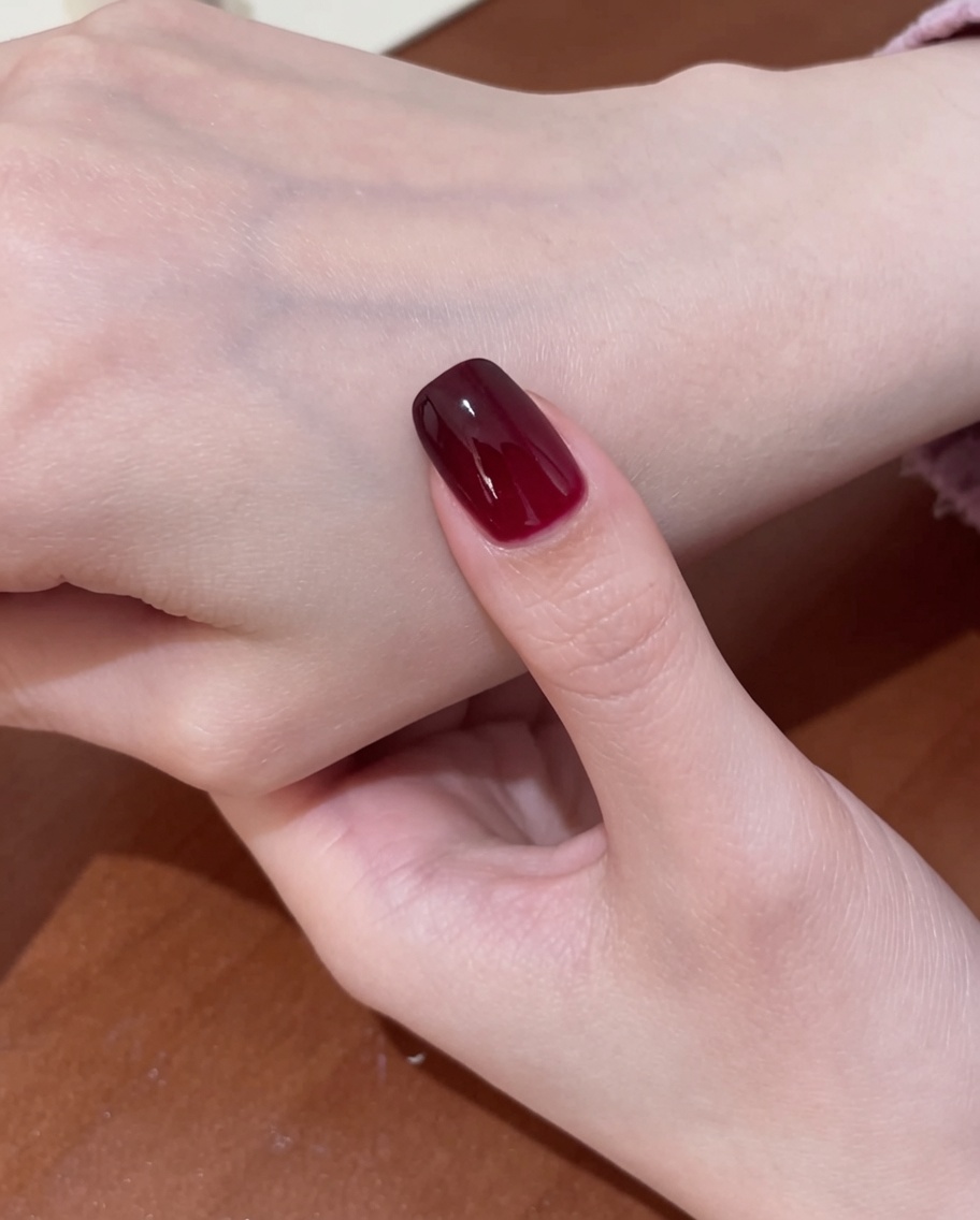 Pędzelek nakładający przezroczysty, błyszczący top coat na gotowy wzór czerwonych paznokci cat-eye.