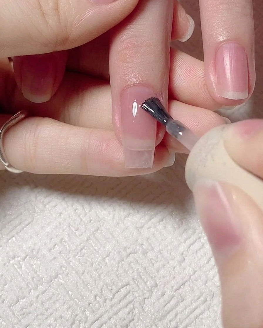Zbliżenie na pędzelek aplikujący półtransparentny żel jelly pink na przygotowaną naturalną płytkę paznokcia.