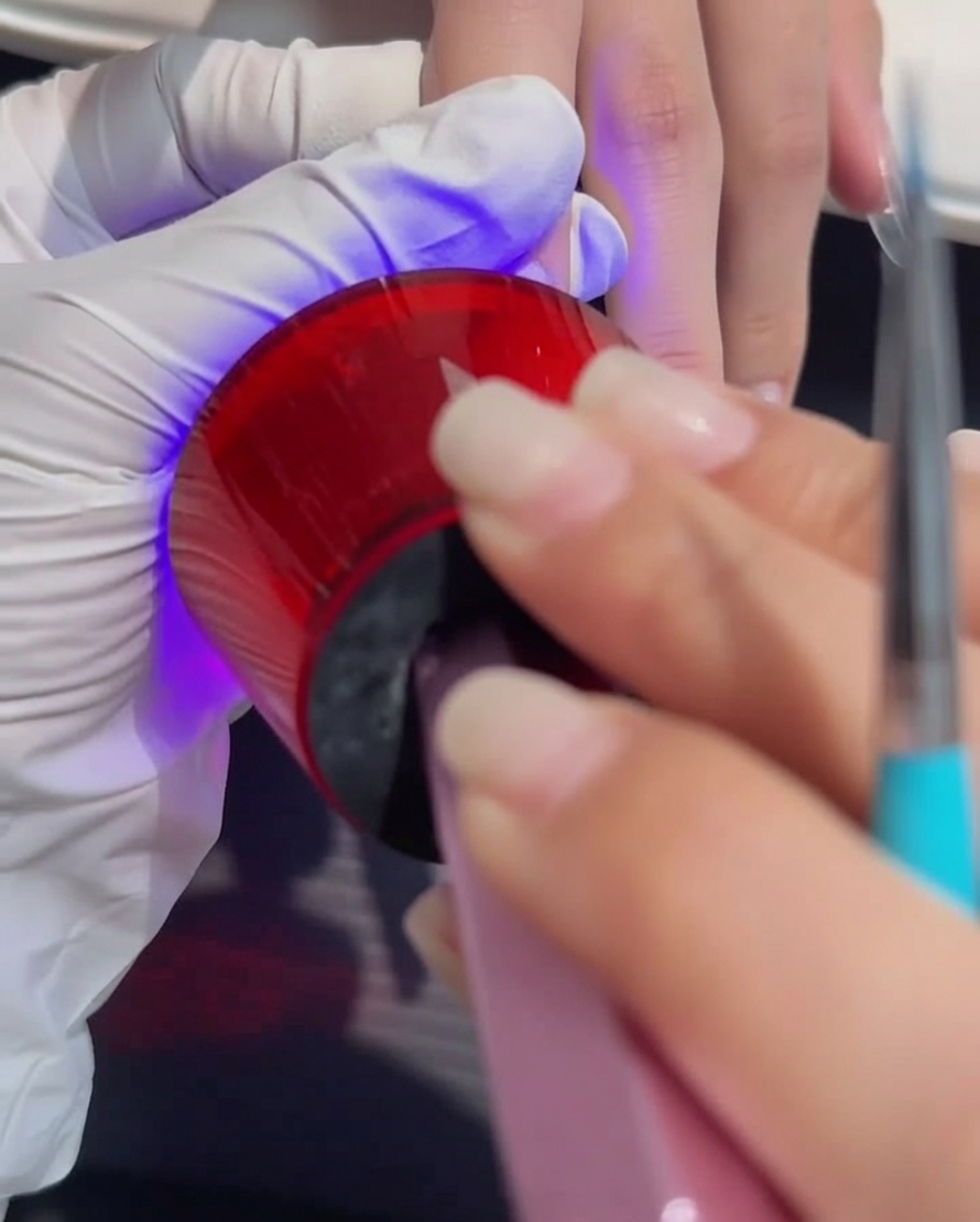 Dłoń umieszczona pod profesjonalną lampą UV/LED podczas procesu utwardzania.