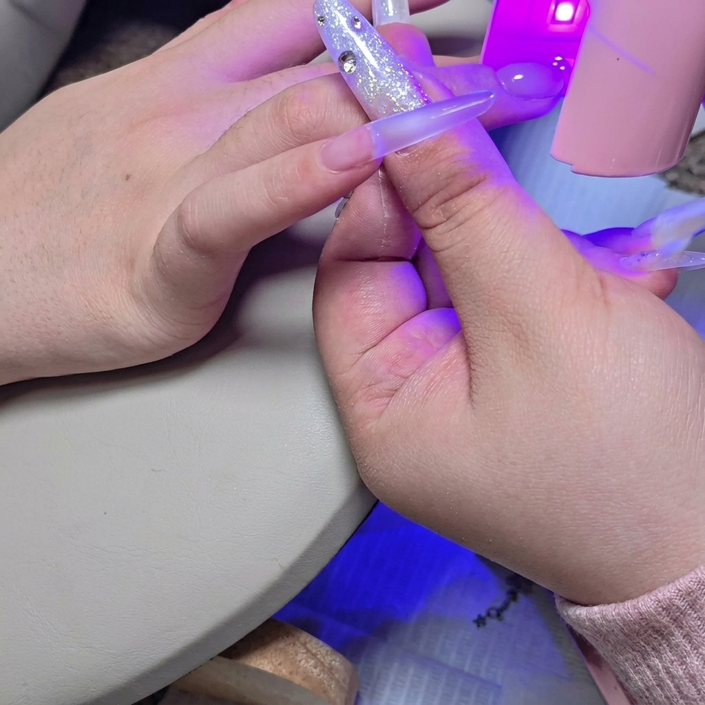 Mała lampa UV/LED nad paznokciem utwardzająca drugą warstwę żelu.