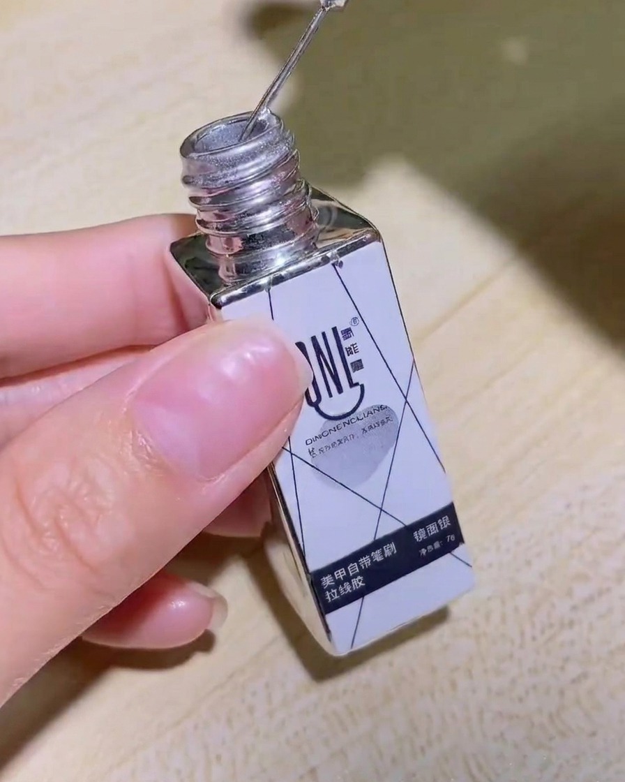 Dłoń trzymająca butelkę srebrnego lustrzanego żelu liner, z wyraźnie widoczną etykietą produktu.
