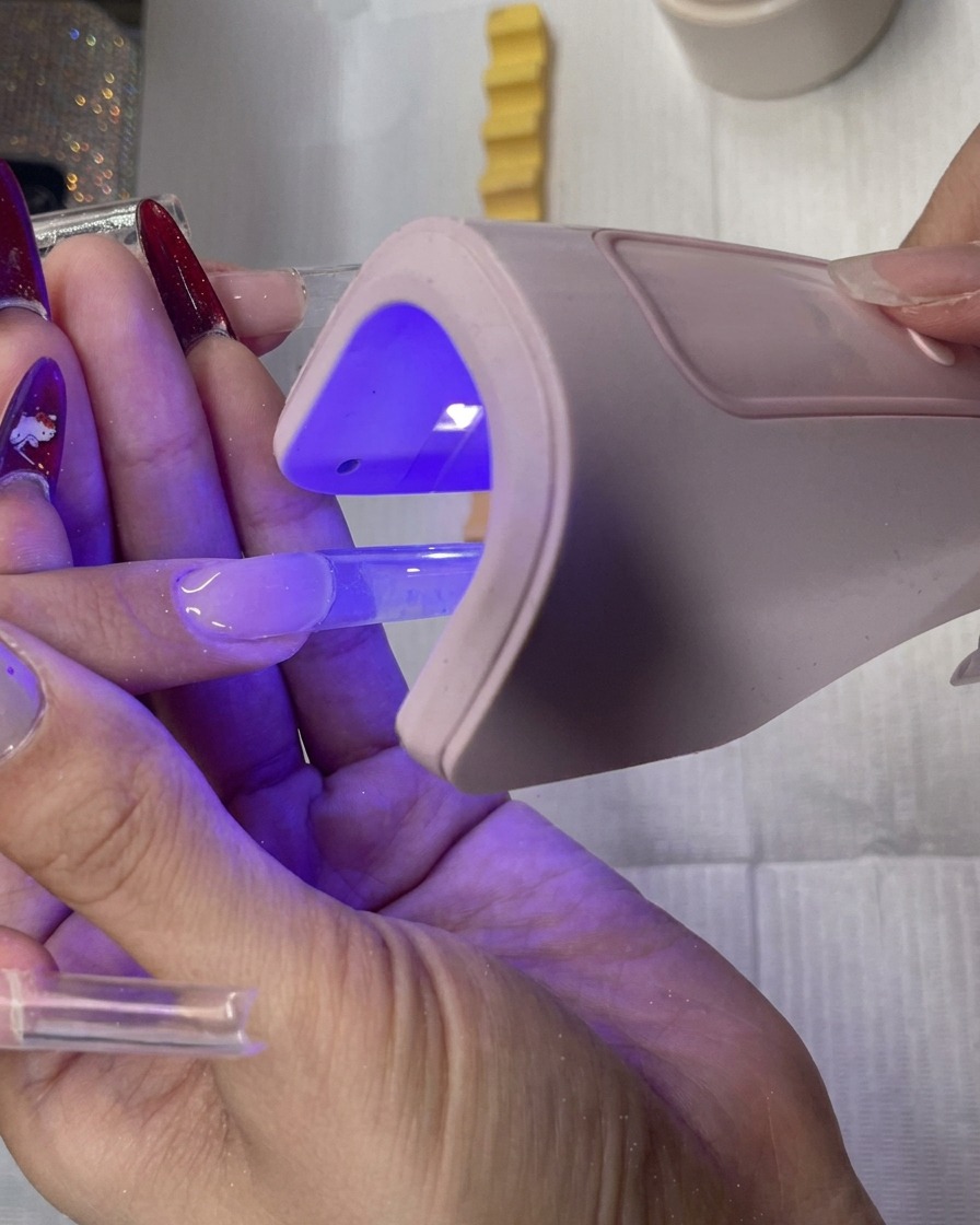 Stylistka używająca małej lampy LED do utwardzenia przedłużenia.