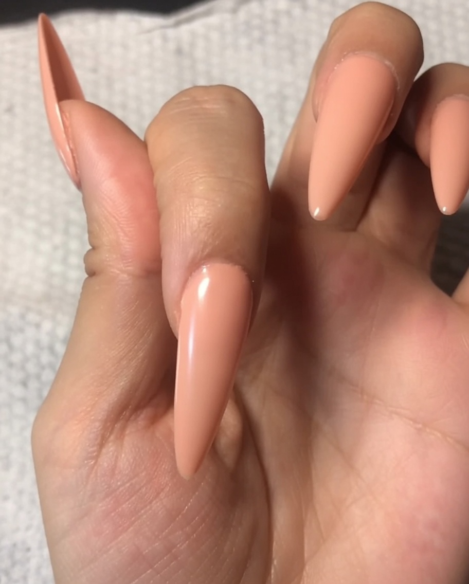 Pędzelek nakładający przezroczysty, błyszczący top coat na paznokieć pomalowany wcześniej na delikatny kolor nude.