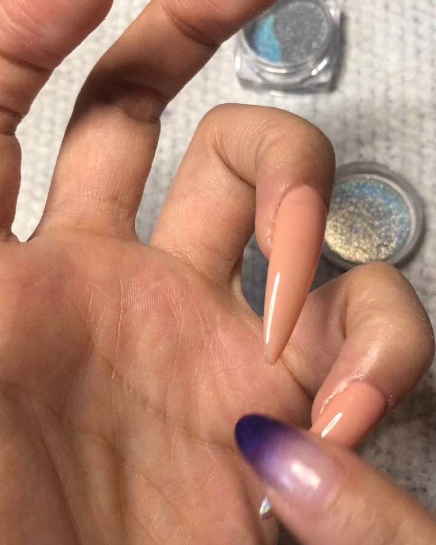 Czysty opuszek palca delikatnie rozcierający granicę holograficznego pyłku ku górze na paznokciu w kolorze nude, tworząc płynny gradient ombre.