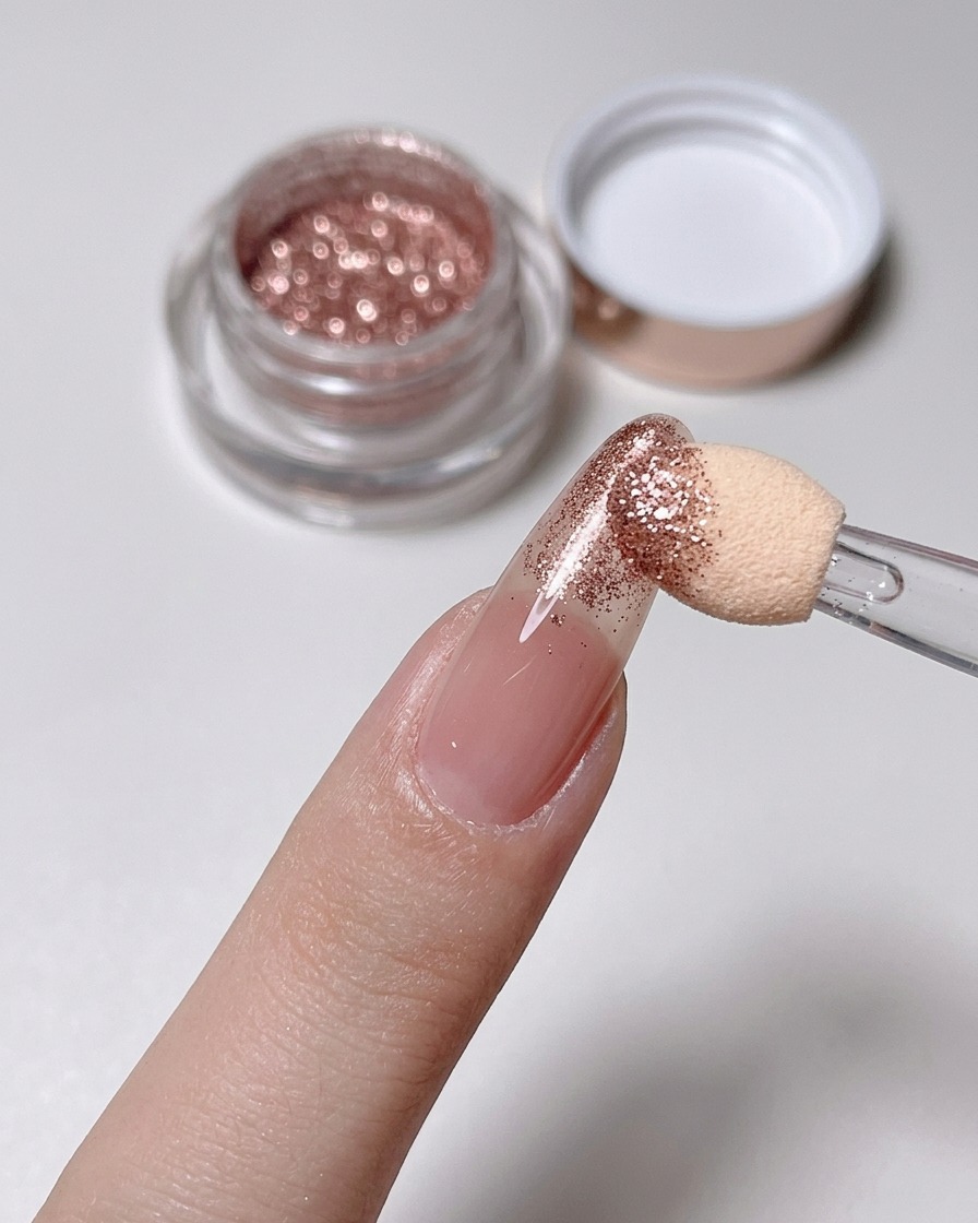 Gąbeczka wcierająca pyłek rose gold w końcówkę paznokcia o kolorze nude.