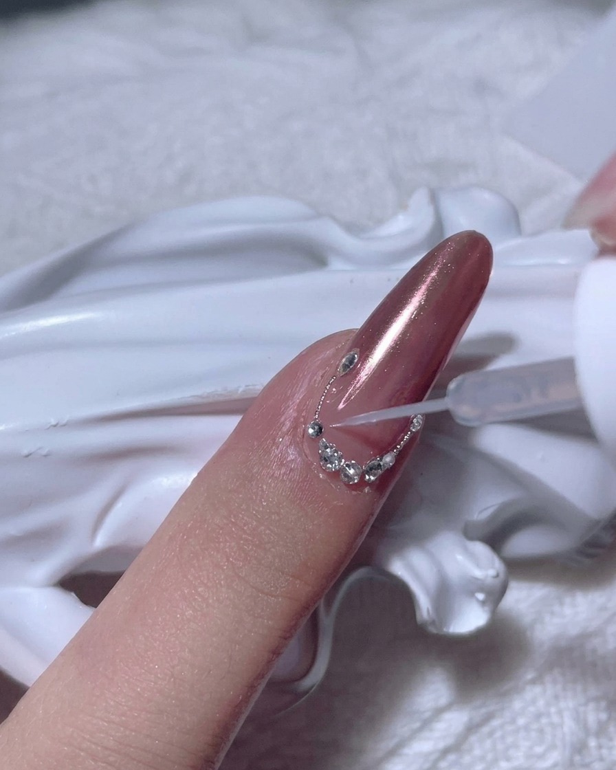 Gotowy łuk z drobnych cyrkonii wzdłuż linii skórek na paznokciu rose gold.