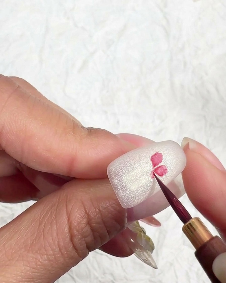 Cienki pędzelek malujący środek różowego kwiatka na matowej powierzchni.
