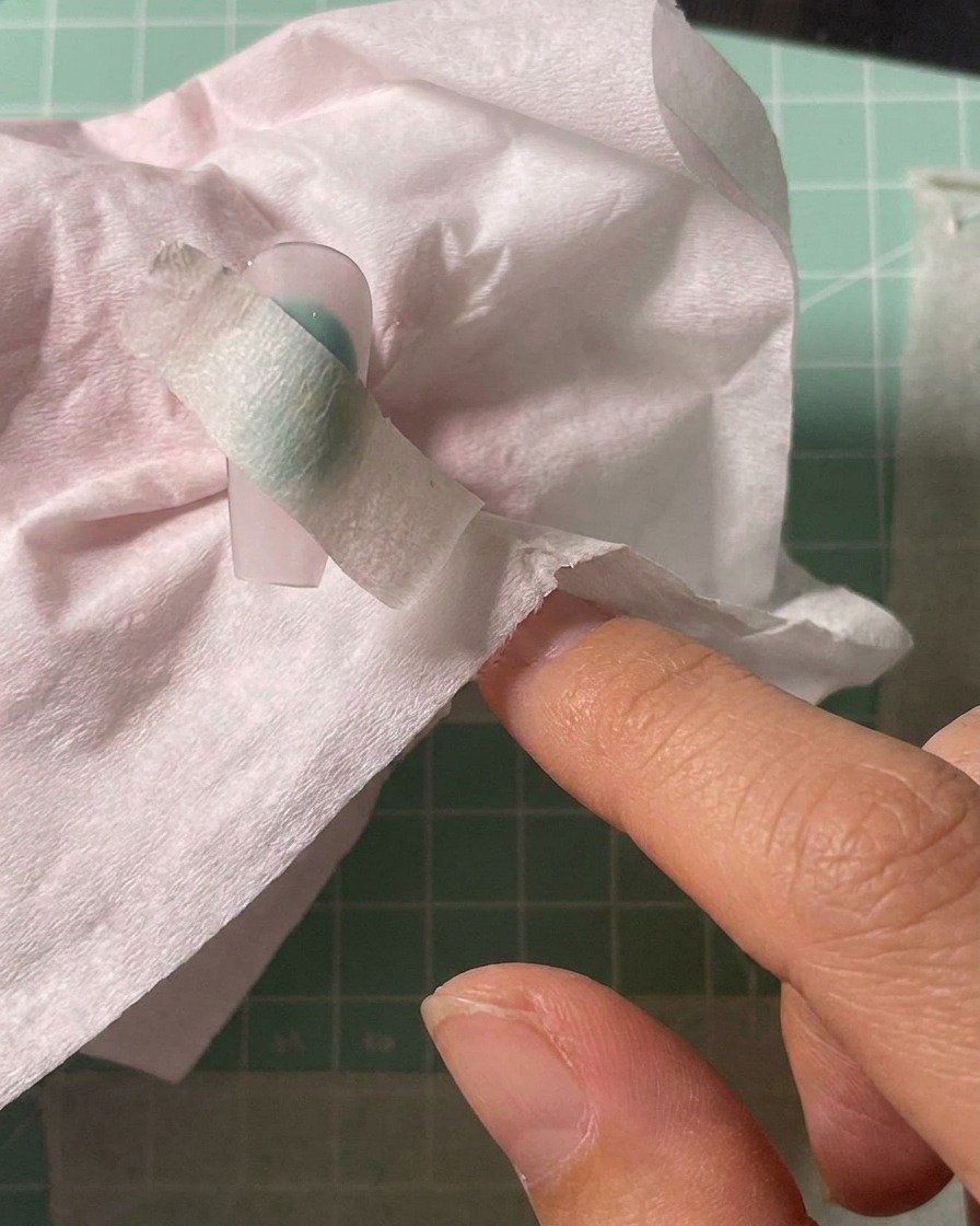 Airbrush nakładający biały pigment na środek zabezpieczonego szablonem tipsa.