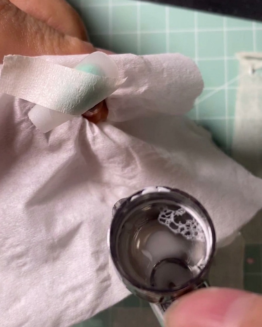 Airbrush rozpylający biały pigment na tips trzymany nad ochronną chusteczką.
