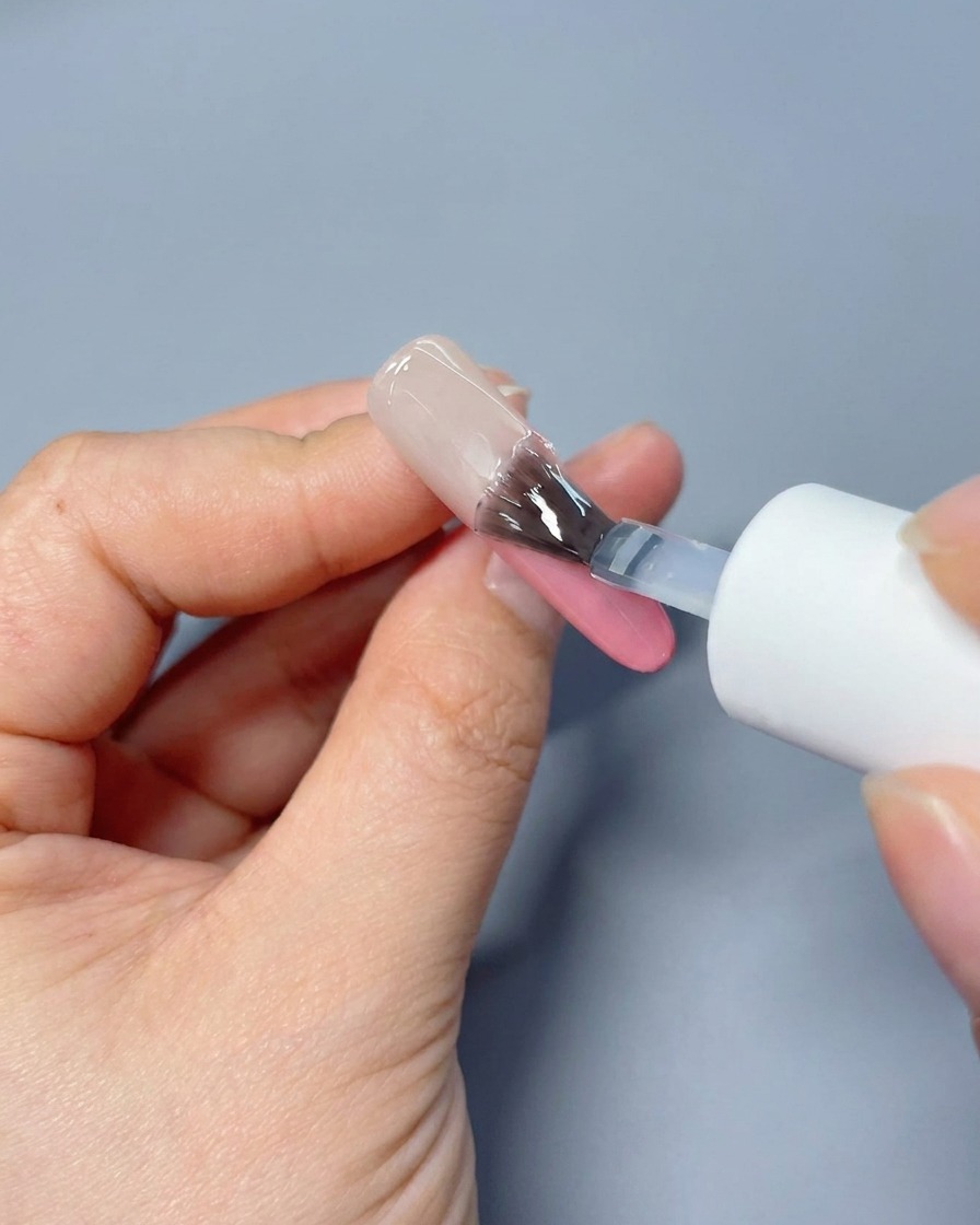 Pędzelek nakładający przezroczysty, błyszczący top coat na różowy gradient na paznokciu.