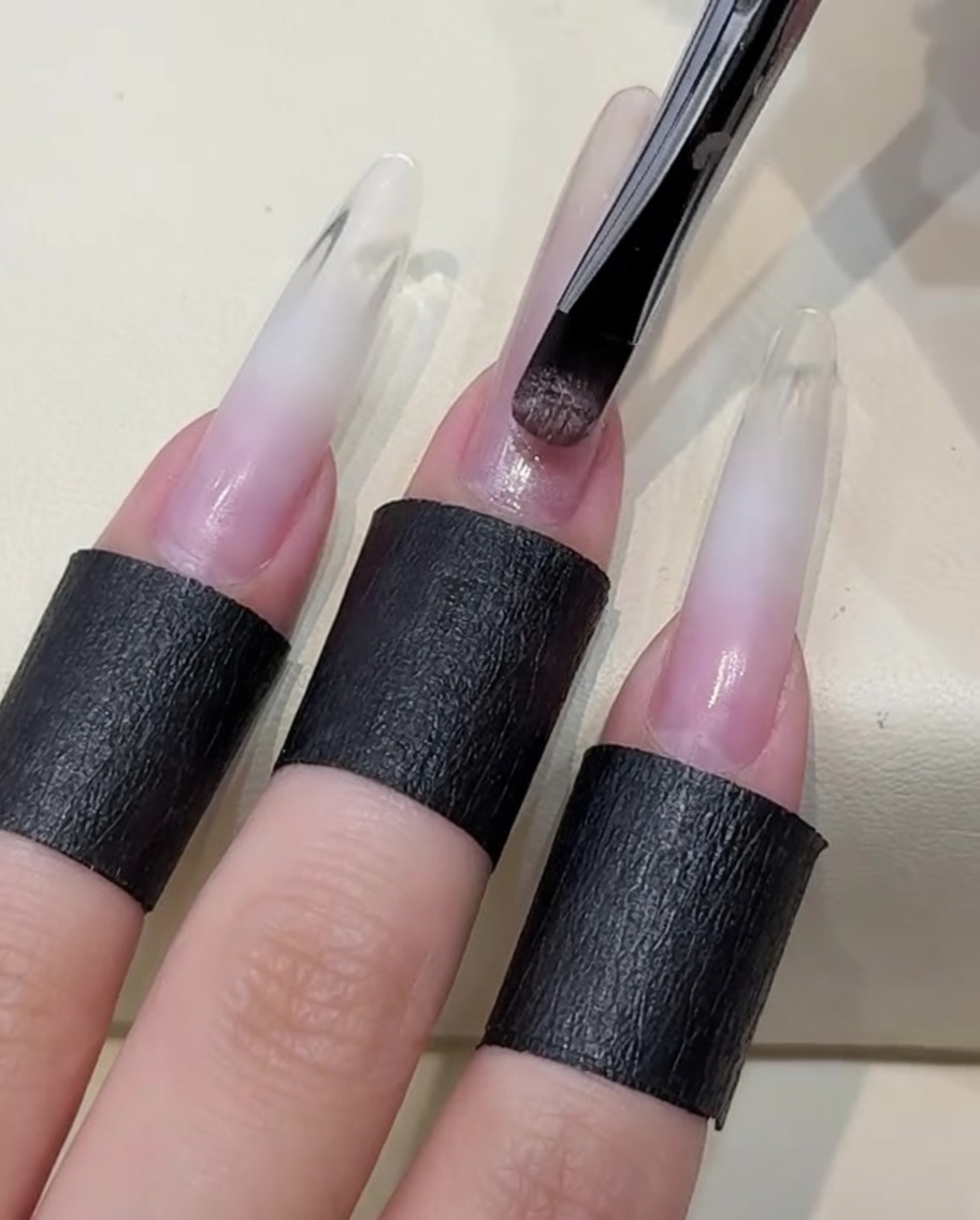 Pędzelek nakładający warstwę jasnego, cielistego lakieru żelowego cat-eye na paznokieć.