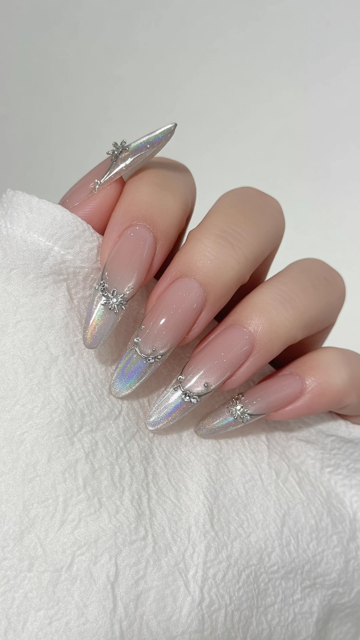 Długie paznokcie o kształcie migdałków z bazą cat-eye w odcieniu nude, wykończone efektem aurora chrome oraz delikatnymi kryształowymi zdobieniami.