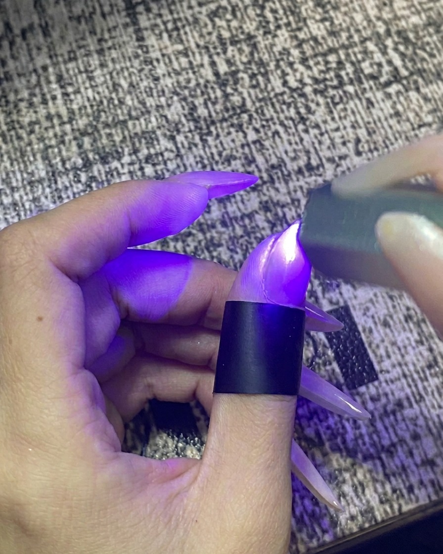 Palec umieszczony w przenośnej lampie UV/LED do paznokci z włączonym światłem.