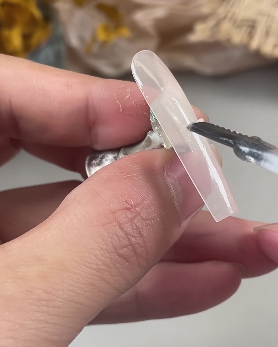 Dłoń używająca narzędzia do ostrożnego nakładania opalizujących, holograficznych płatków brokatu na mokry, nieutwardzony żel na tipsie.