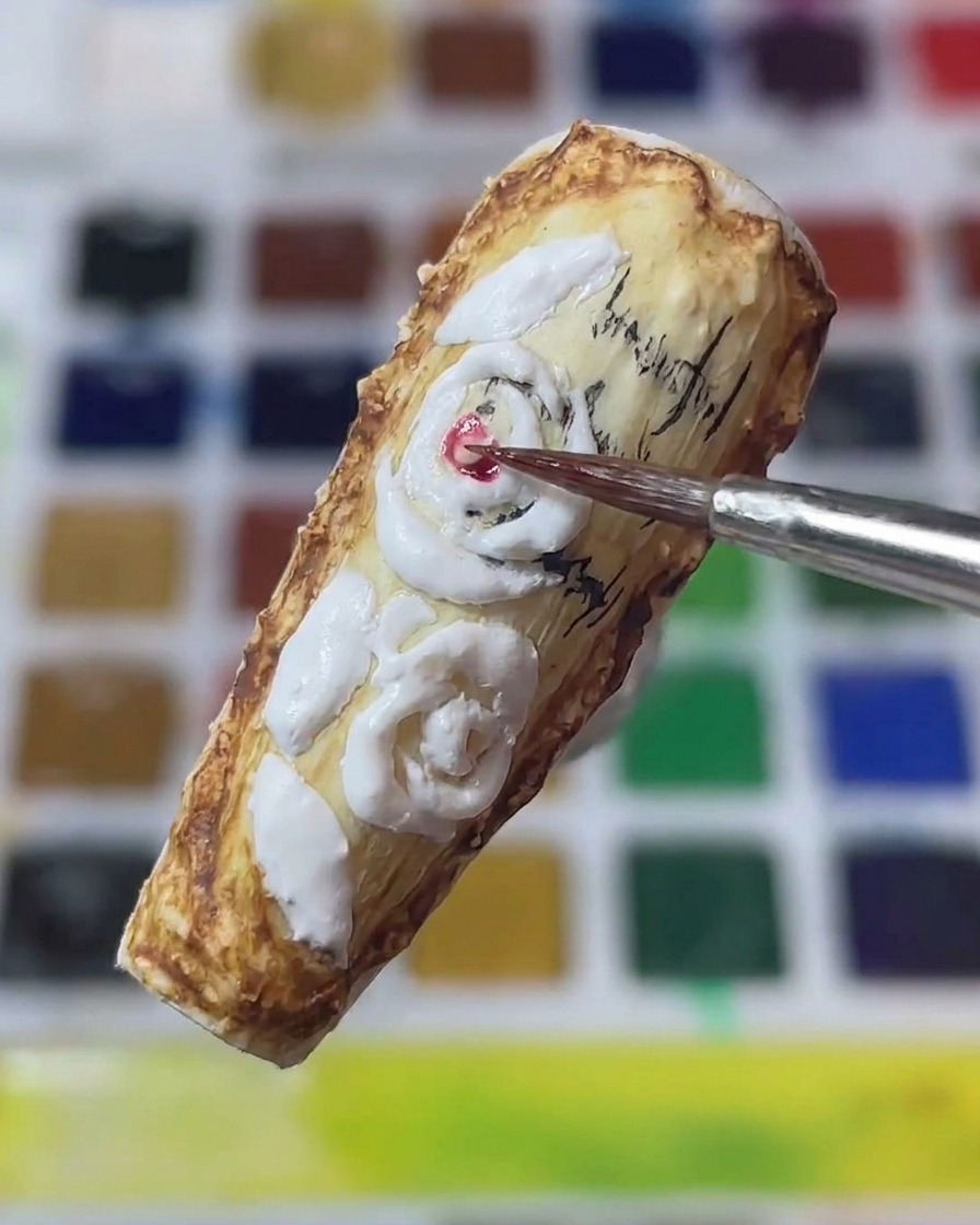 Zbliżenie na precyzyjny pędzelek nakładający czerwony pigment na środek białych, wyrzeźbionych róż 3D na paznokciu w stylu vintage.