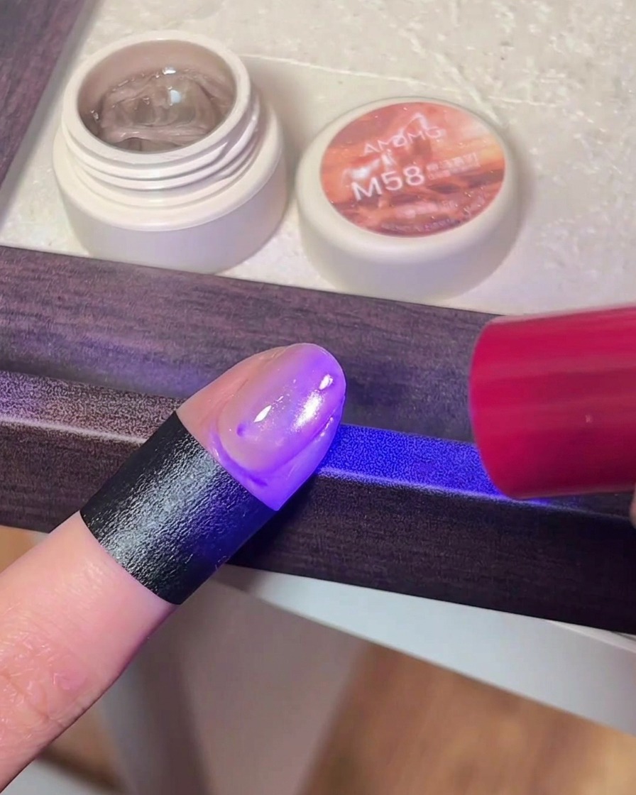 Zbliżenie na paznokieć z żelem cat eye pod fioletowym światłem lampy UV/LED.