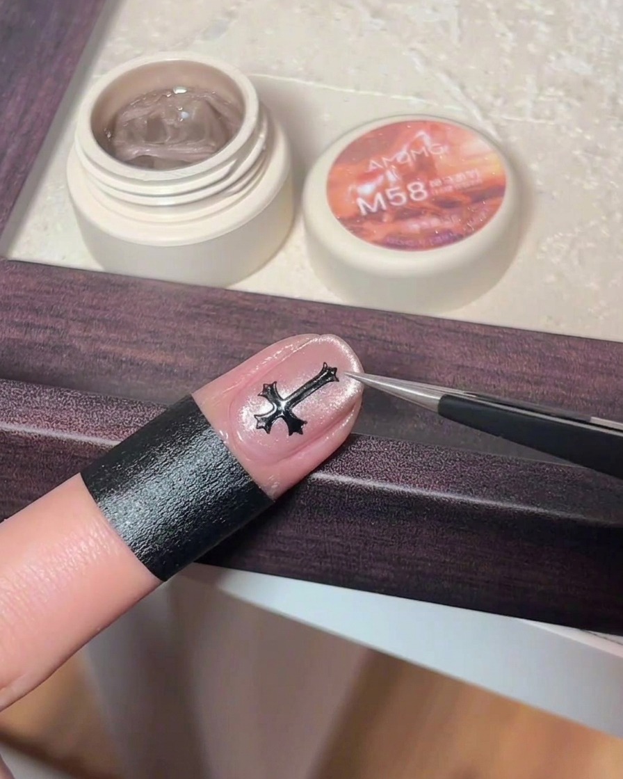 Pęseta umieszczająca mały, czarny metalowy krzyżyk na środku paznokcia z różowym efektem cat eye.