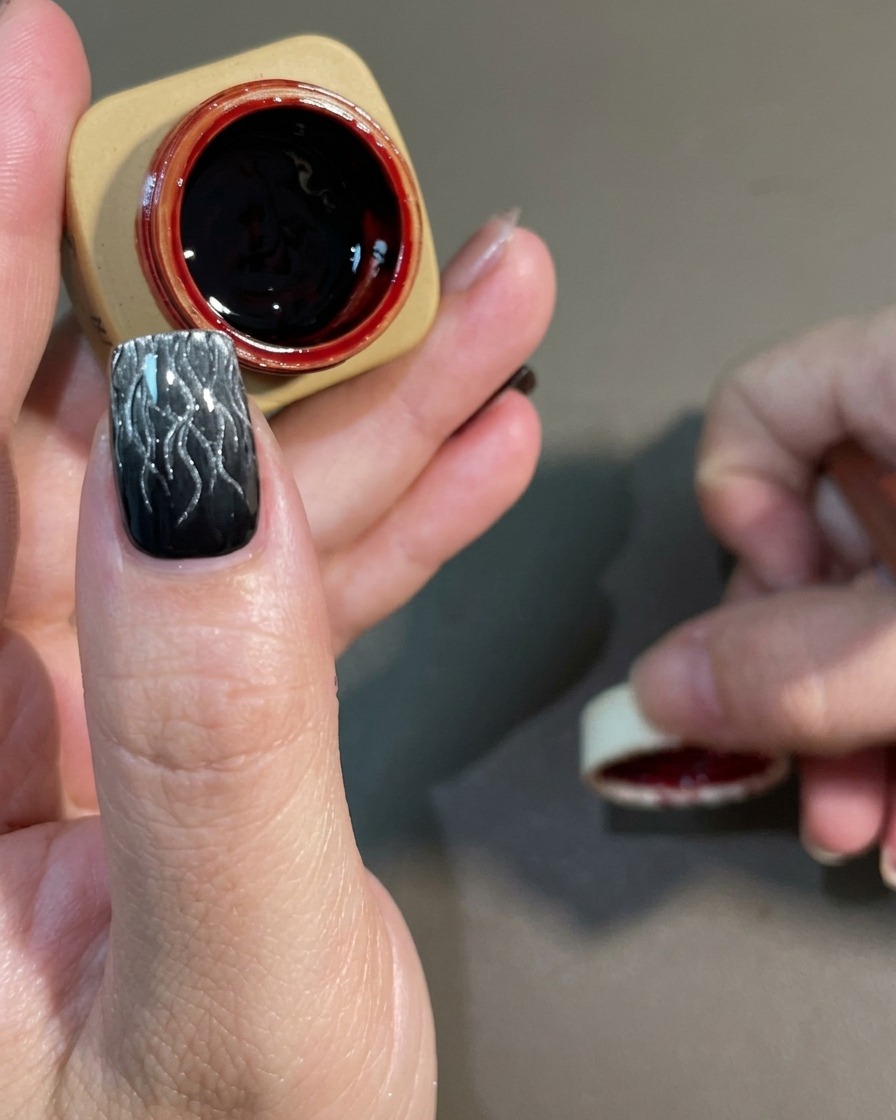 Pędzelek nakładający półprzezroczysty, ciemnoczerwony lakier na utwardzony czarno-biały wzór.