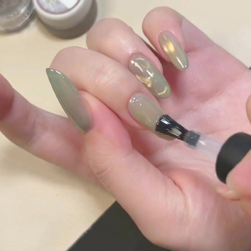 Pędzelek aplikujący bezbarwny, matowy top coat na zielony paznokieć cat eye.