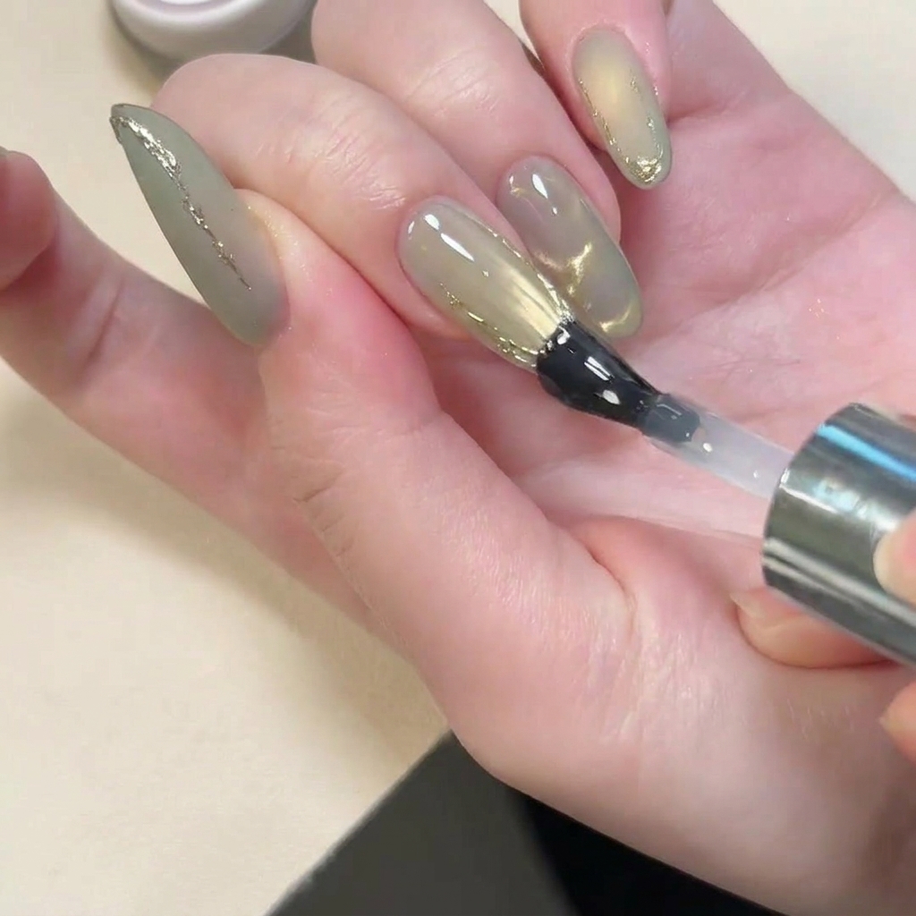 Pędzelek aplikujący błyszczący top coat na paznokieć z matowym wykończeniem i złotymi akcentami 3D.