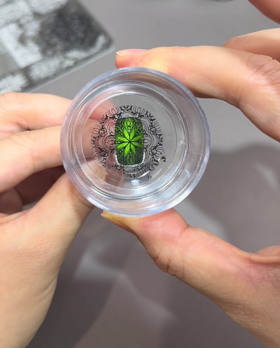 Spojrzenie prosto z góry przez przezroczysty stempel silikonowy, pokazujące skomplikowany czarny wzór idealnie dopasowany do jaskrawozielonego paznokcia cat eye.