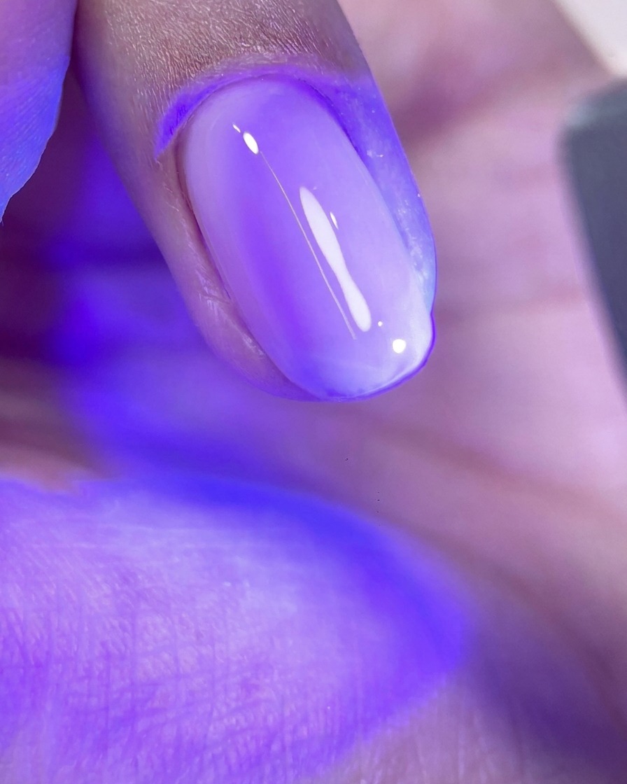 Paznokieć z nieutwardzoną warstwą lśniącego różowego żelu spoczywający pod fioletowym światłem lampy UV/LED.