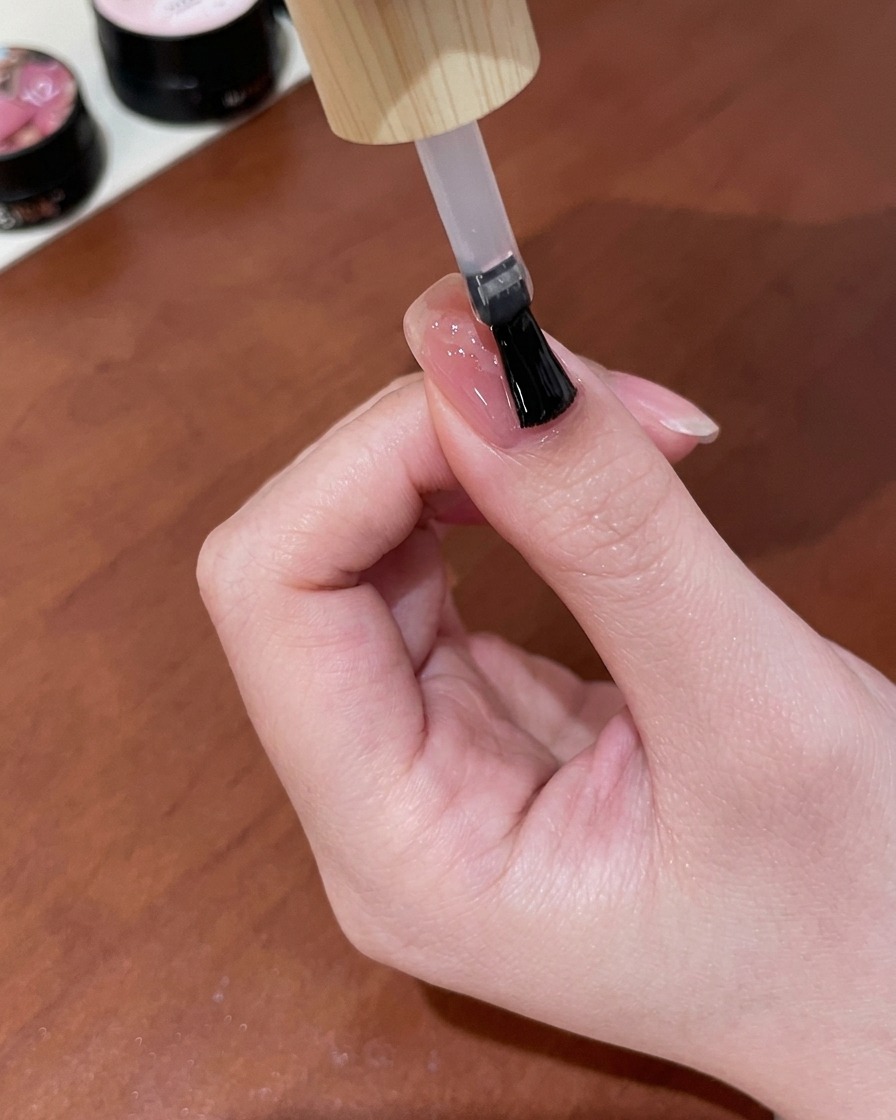 Pędzelek nakładający błyszczący top coat na gotowy manicure z motylem.