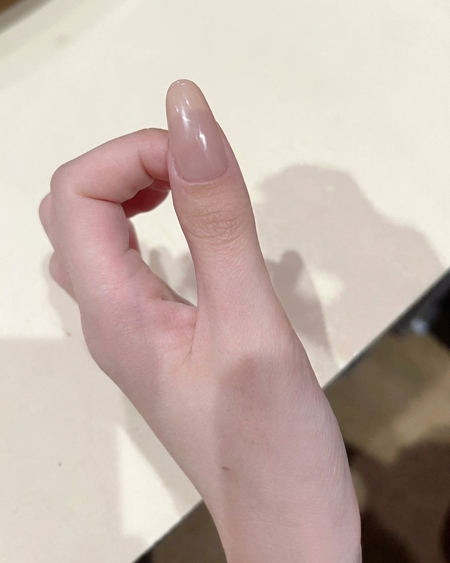 Zbliżenie na pędzelek precyzyjny umieszczający małą, skoncentrowaną kropkę różowego żelu na środku paznokcia nude.