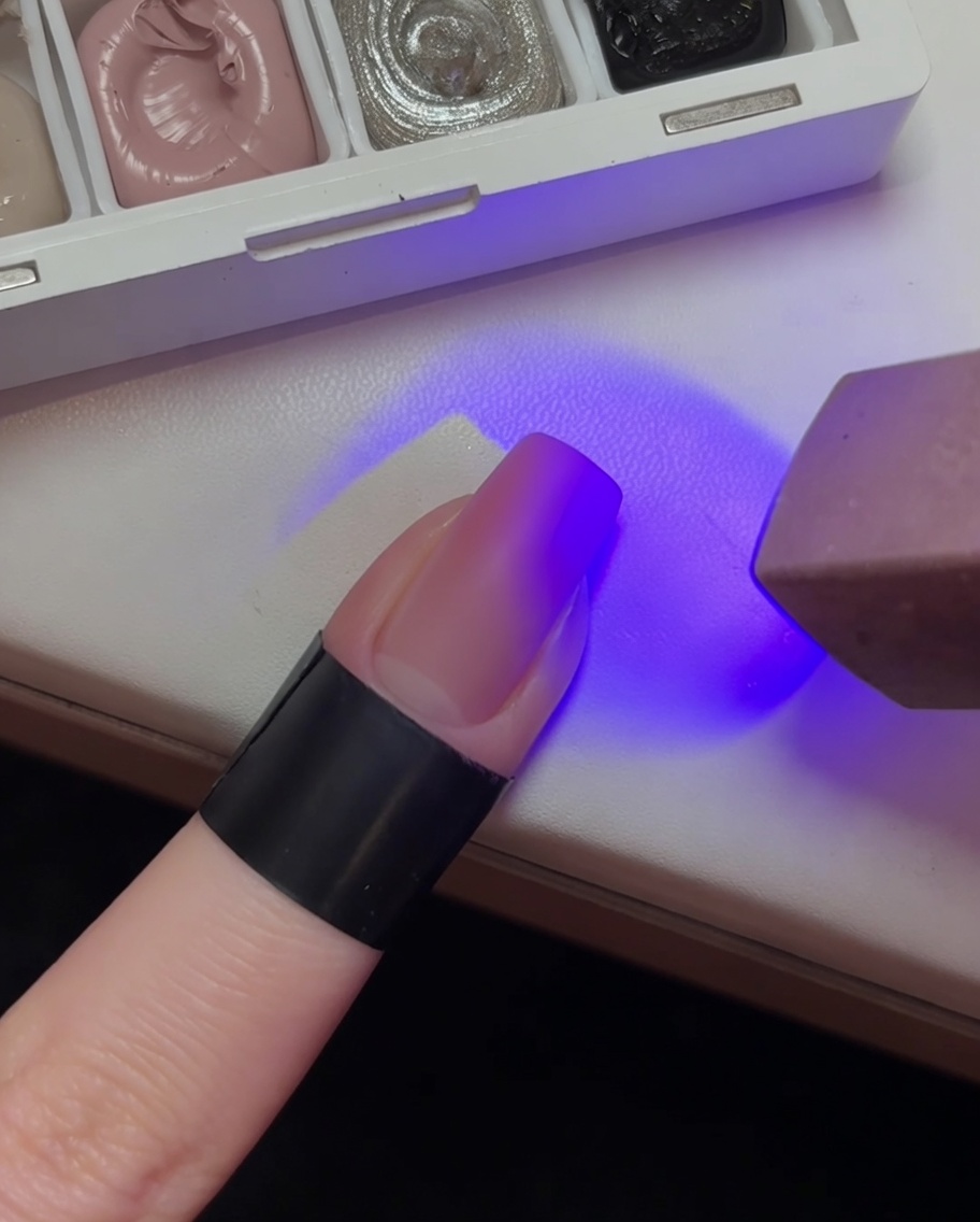 Paznokieć z jasnoróżową bazą ombre utwardzany pod fioletowym światłem lampy UV.