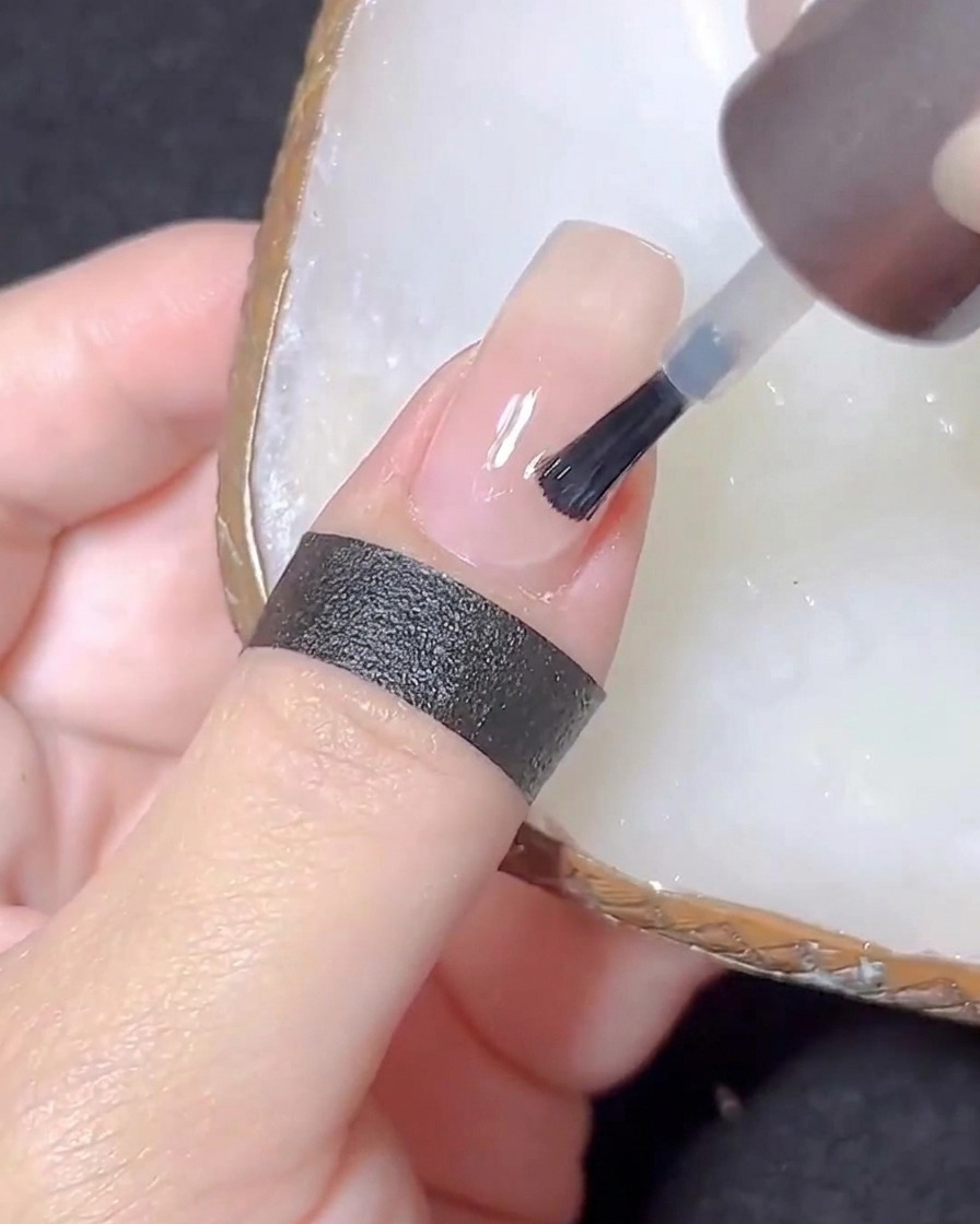 Pędzelek aplikujący bezbarwny top coat na paznokieć w kolorze nude.