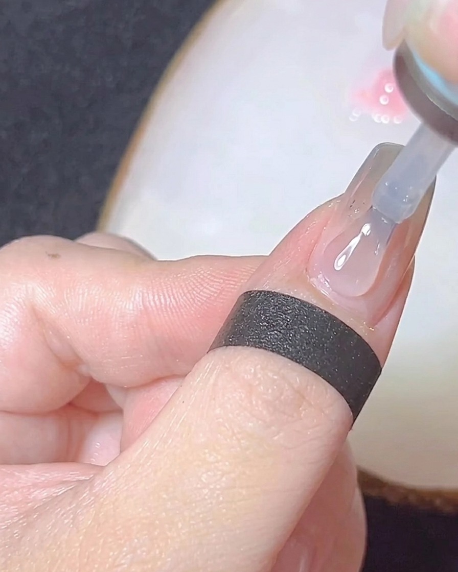 Zbliżenie pędzelka nakładającego nabłyszczający top coat na chromowane paznokcie.