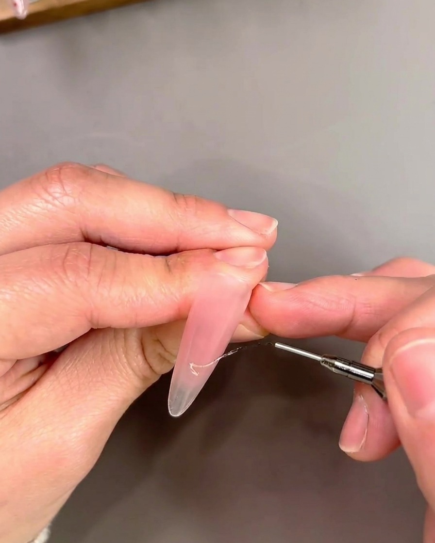 Zbliżenie na pędzelek typu liner nakładający złoty lakier cat-eye w formie końcówki French.