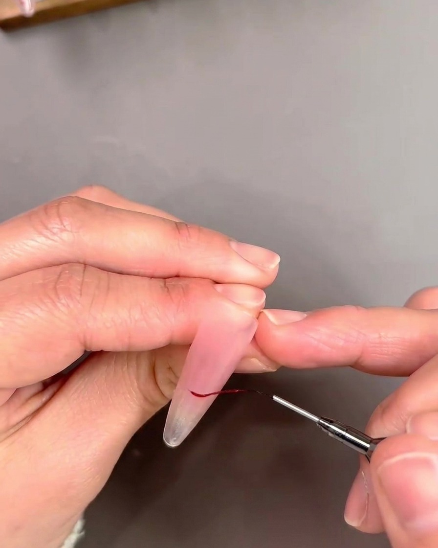 Zbliżenie na pędzelek typu liner obrysowujący końcówkę French czerwoną linią.