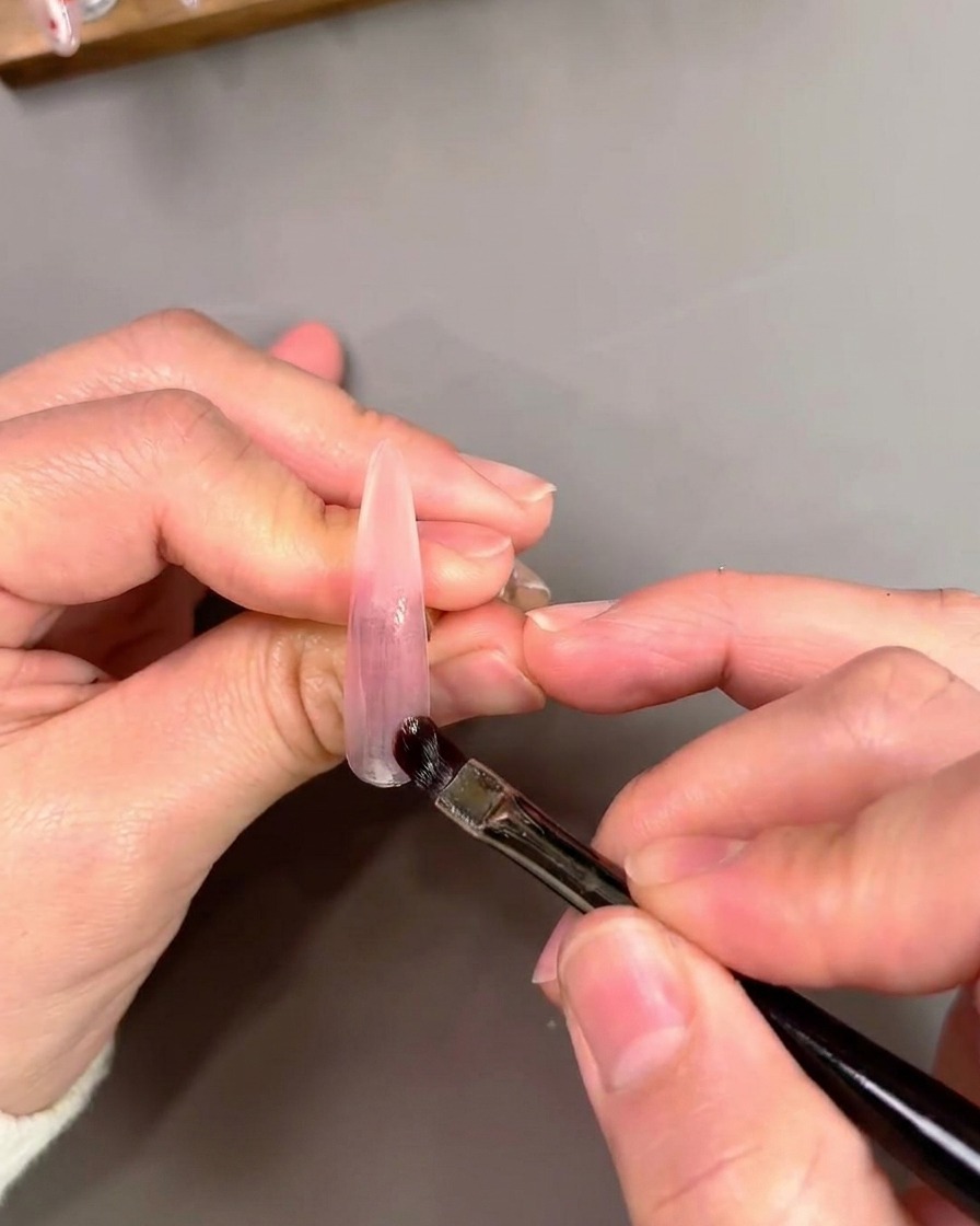 Płaski pędzelek nakładający i blendujący fioletowy lakier cat-eye na sztuczny tips.