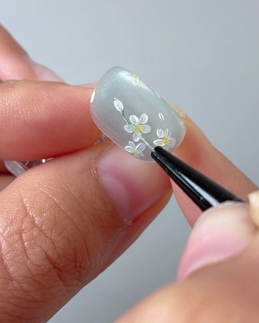 Zbliżenie na pędzelek rysujący cienką zieloną łodygę na bazie cat-eye.