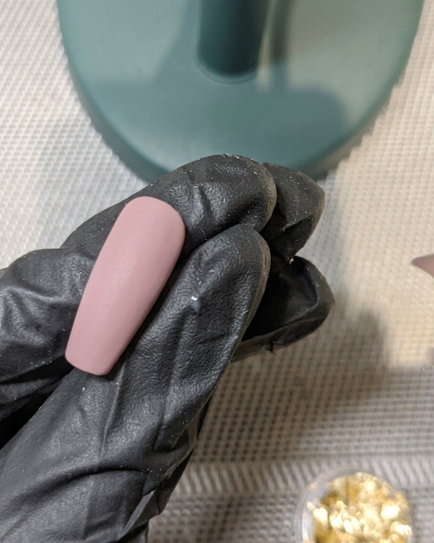 Pędzelek aplikujący matowy top coat na paznokieć z zatopioną złotą folią.