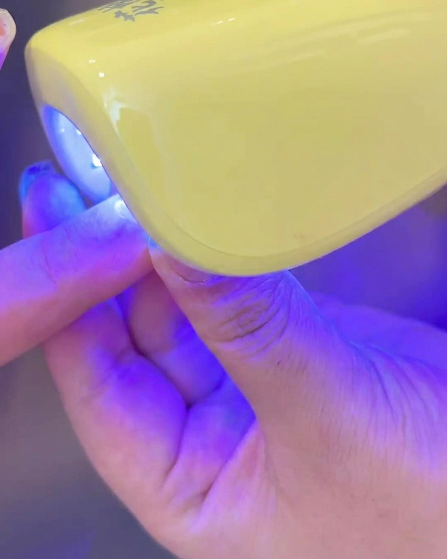 Dłoń umieszczająca paznokieć z nałożonym mlecznym żelem pod lampą UV/LED.