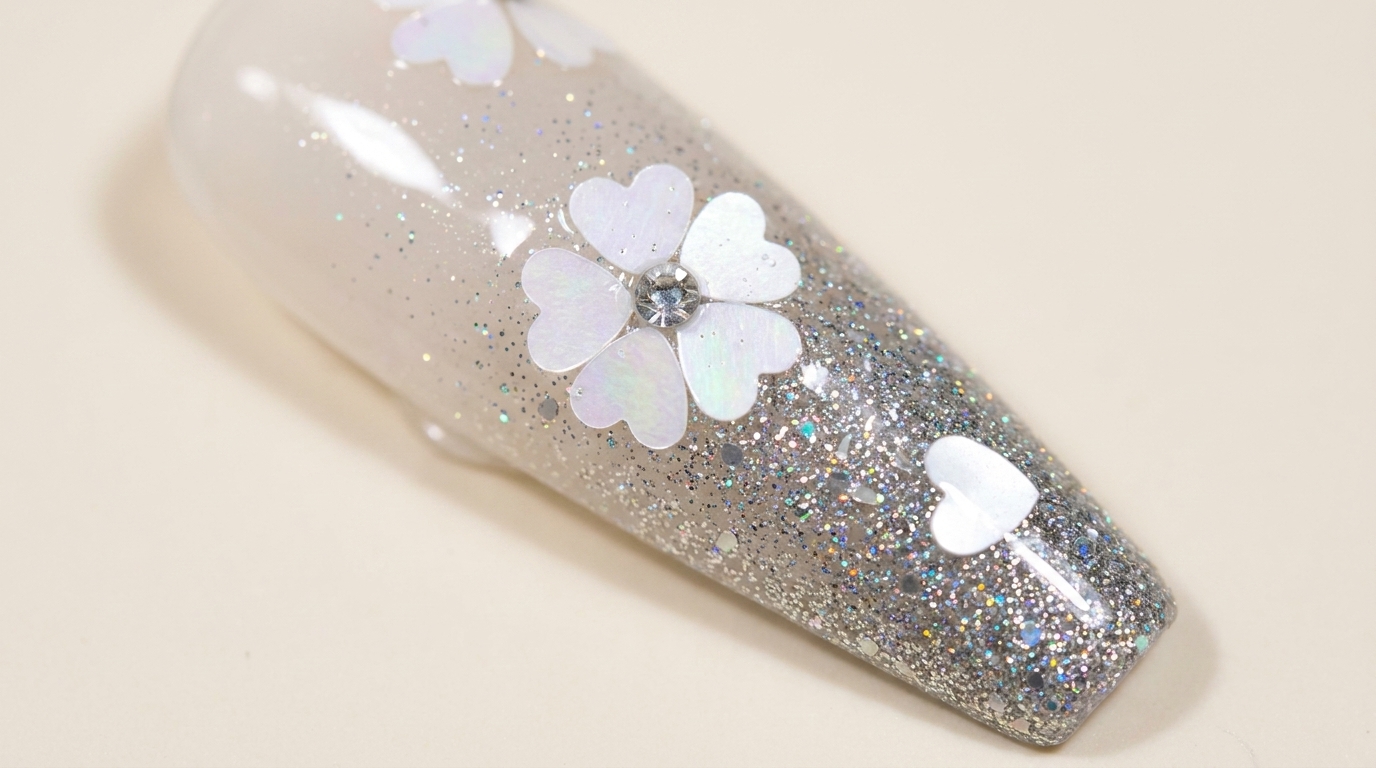 Zjawiskowy manicure z motywem kwiatów wiśni, srebrnym blaskiem, delikatnymi cekinami i kryształowym środkiem.