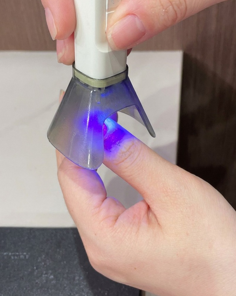 Palec trzymany pod lampą UV w ostatnim kroku utwardzania manicure.